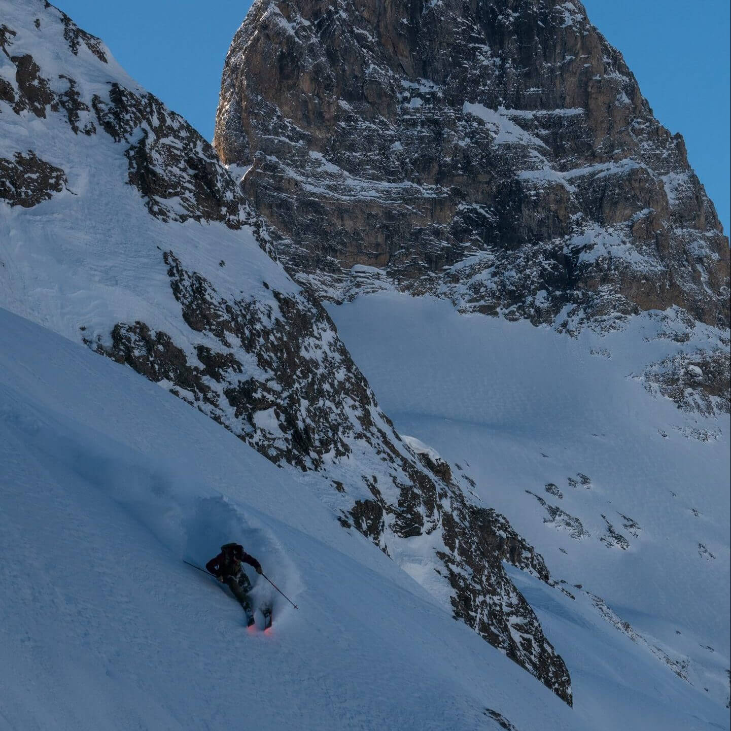 Skier skiing powder under a large rock face