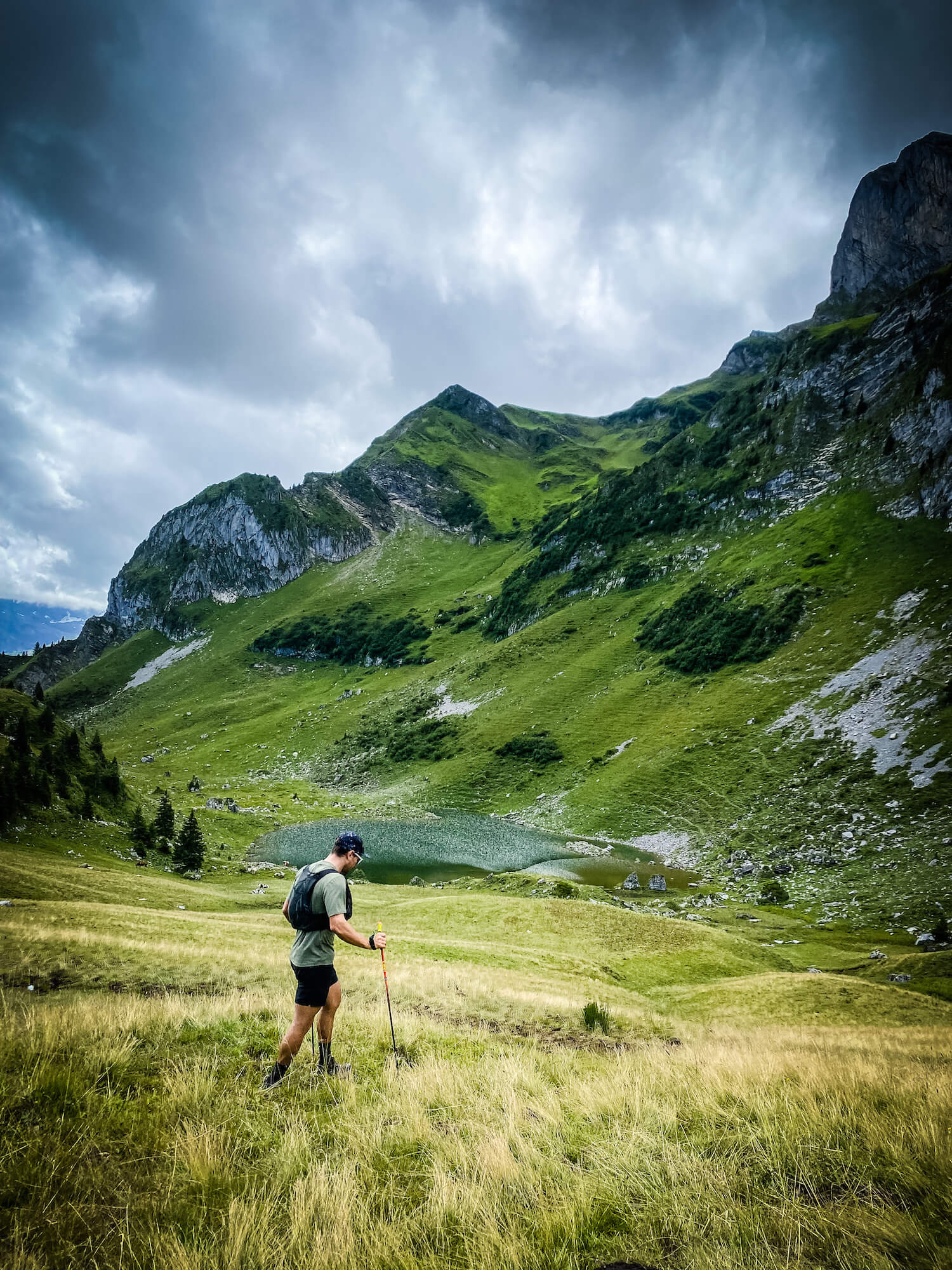 Hiker walking through grass field in the mountains in front of alpine lake.