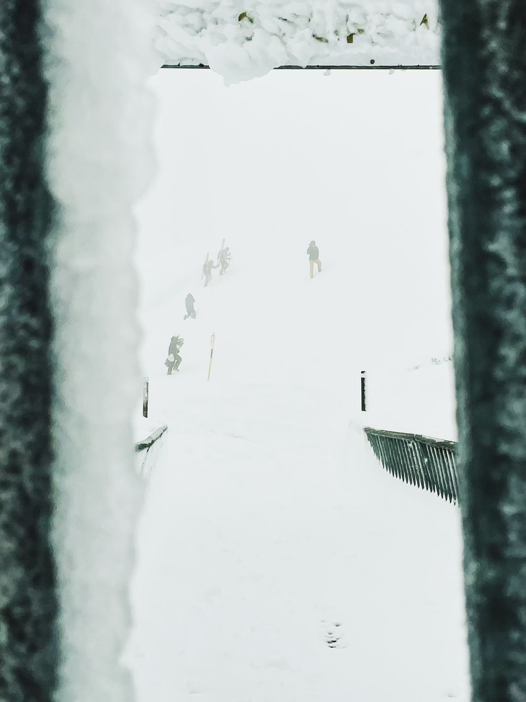 Foggy, snowy scene from a window with skiers and photographers in the background 