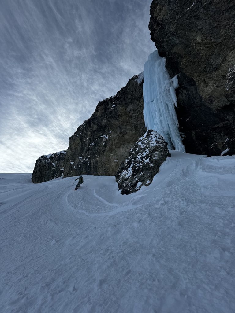 Skier making a turn next to a large ice waterfall.