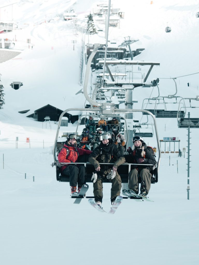 Skiers sitting on a chairlift, smiling at the camera