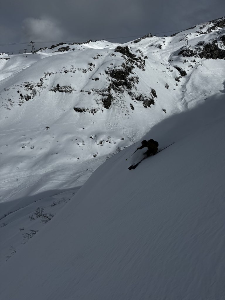 Skier making a turn in front of a beautiful mountain in the shadows.