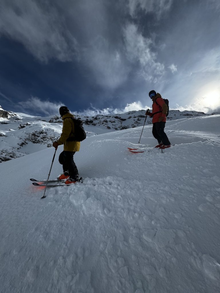 Skiers standing on a mountainside in snow looking at the clouds.